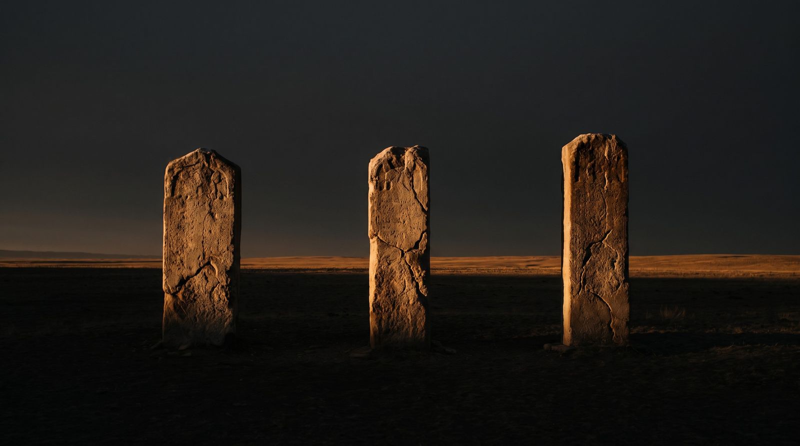 Three stone stelae on a plain in the light of dawn